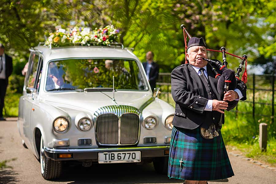 Bagpiper leading funeral procession with classic hearse